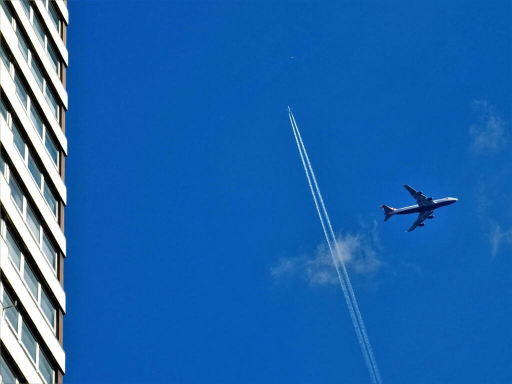 A jet plane with contrail flying high in the sky next to a modern skyscraper.